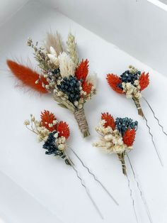 four hair pins with flowers and feathers on them sitting in a white box next to each other