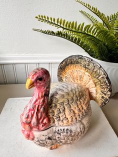 a ceramic turkey sitting on top of a white table next to a potted plant