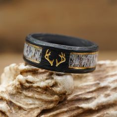 ABOUT THIS RING Material: Black Forged Carbon Fiber, 2 Gold Plated Strips, and a Natural Grain Antler Inlay with a Resin Coating. Color*/Finish: Black and Gold Engraving: Antlers with Gold Oil Width: 8mm *All Antler Rings are 100% Unique so color may vary slightly from image shown. Check out the information about our Antler Rings for more details! QUESTIONS ABOUT SIZING Go to our Ring Sizing Guide for details and important guidance. OTHER BENEFITS FOR YOU FREE ACTIVITY BAND with Purchase (a $55 Hunting Wedding Rings For Men, Antler Engagement Ring, Deer Antler Wedding Band, Deer Antler Wedding, Antler Rings, Antler Wedding Rings, Antler Wedding Band, Deer Antler Ring, Hunter Wedding