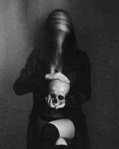 black and white photograph of a woman with a skull on her chest sitting in front of a wall