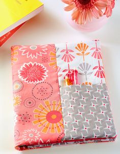 a pink and grey notebook cover sitting on top of a table next to a flower vase