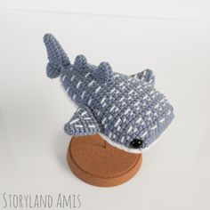 a crocheted toy shark sitting on top of a wooden stand with a white background