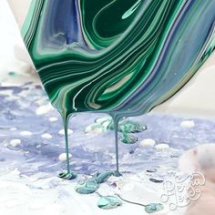 a green and blue liquid pouring out of a white vase on top of a table