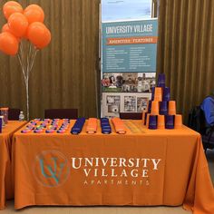 an orange table topped with balloons in front of a sign that says university village apartments