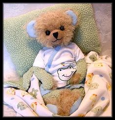 a brown teddy bear sitting on top of a bed next to a pillow and blanket