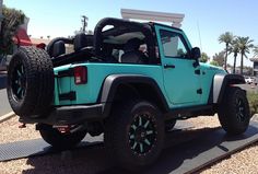 a turquoise jeep with black wheels parked on the side of train tracks in front of palm trees