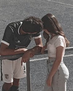 a man and woman standing next to each other on top of a parking lot near a fence