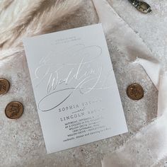 a white wedding card on top of a pile of coins next to a pair of scissors