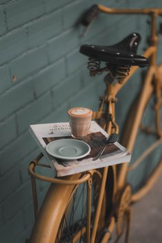 a bicycle parked next to a brick wall with a cup of coffee on the front