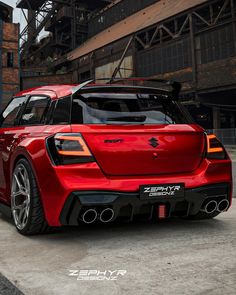 the rear end of a red sports car parked in front of an industrial area with buildings