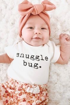 a baby girl with a pink bow on her head wearing a tshirt that says snuggle bug