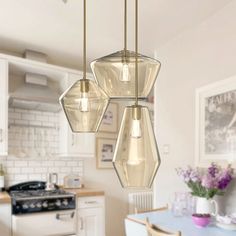 three lights hanging from a kitchen ceiling over a dining room table with chairs and a stove