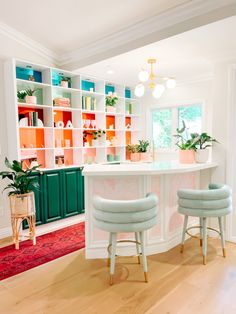 two stools sit in front of an island with bookshelves and plants on it