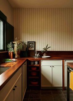 a kitchen with wooden counter tops and white cabinets, along with potted plants in the corner