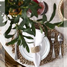 the table is set with white plates, silverware and green leaves on it's placemats