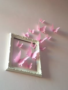 some pink butterflies are flying out of a white frame on the wall in front of a mirror