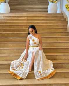 a woman is sitting on the steps wearing a white and gold dress with yellow flowers