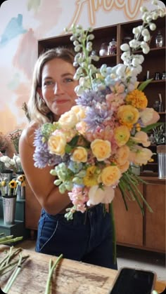 a woman holding a bouquet of flowers in front of a wooden table with other items on it