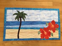 a quilted placemat with a palm tree and flowers on it, along with the ocean