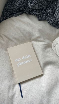 a book sitting on top of a bed next to an unmade blanket with the words my daily planner written on it