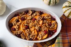 a white bowl filled with fruit and nuts on top of a table next to pumpkins