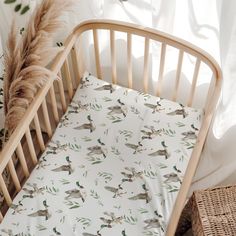 a baby crib with a white sheet and green birds on it's side