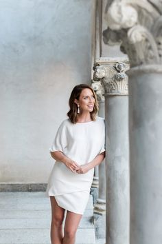 a woman standing next to a column in a white dress