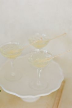 two martini glasses sitting on top of a white platter next to a green plant