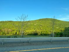 an empty highway in front of a mountain with trees on the side and hills behind it