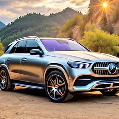 a silver mercedes benz suv parked in front of a mountain range with the sun behind it