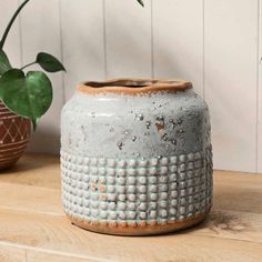 a white vase sitting on top of a wooden table next to a potted plant