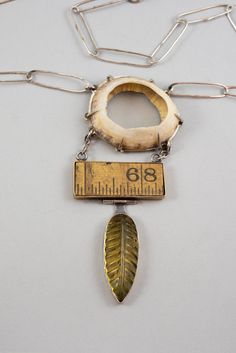 Three seemingly unrelated objects; an amber leaf, a segment of a wooden ruler, and a found shell, are hung together juxtaposing textures, shapes and sizes. While maybe showing similar characteristics. Hand made chain and clasp. Mixed metals and one of a kind. Artsy Silver Necklace With Unique Variations, Artistic Necklaces With Unique Variations, Artsy Pendant Necklace With Unique Variations, Unique Multi-strand Metal Necklace, Silver Brutalist Metal Necklace, Antler Jewelry, Found Object Jewelry, Textile Necklace, Fossil Jewelry