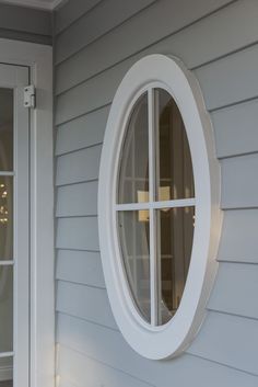 an oval window on the side of a house with white siding and trim around it