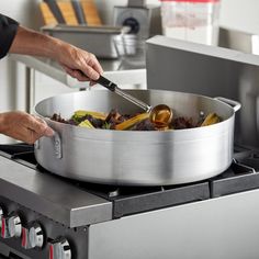 a person stirring food in a large pot on top of the stove with tongs