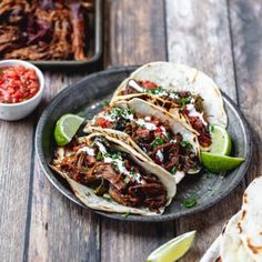 three shredded beef tacos on a plate with salsa and lime wedges next to it