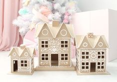 three cardboard houses sitting next to a white christmas tree with pink decorations on the top