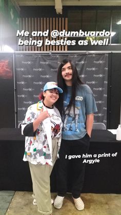 two people standing next to each other in front of a poster