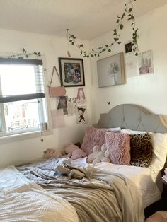 an unmade bed in a bedroom with pictures on the wall and plants hanging from the ceiling