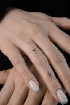 two hands holding each other with tattoos on their fingers and one has a star tattoo on the middle finger