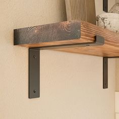 a wooden shelf with two metal brackets on it and a vase in the back ground