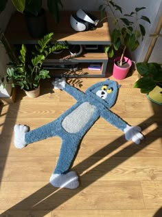 a blue stuffed animal laying on top of a wooden floor next to potted plants