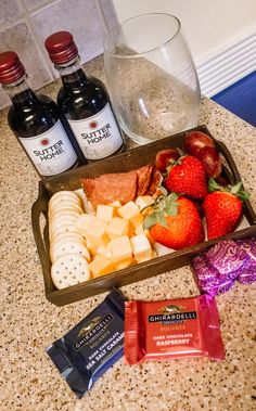 a tray filled with fruit, cheese and crackers next to two bottles of wine