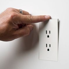 a person is pointing at an electrical outlet on the wall with one hand and two other fingers