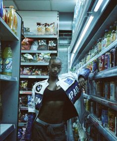 a woman is standing in the aisle of a grocery store holding a bag and reading a newspaper