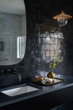 a bathroom with black tiles and gold accents on the countertop, along with a vase filled with flowers