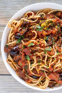 a white bowl filled with pasta and sauce on top of a wooden table next to a fork