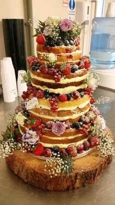 a multi layer cake sitting on top of a wooden table covered in flowers and berries