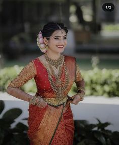 a woman in a red and gold sari with jewelry on her neck, smiling at the camera