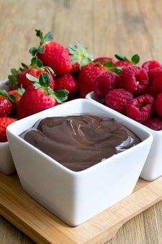 two white bowls filled with chocolate and raspberries on top of a wooden table