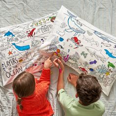 two children are playing with an umbrella on a bed sheet that says layers of the ocean